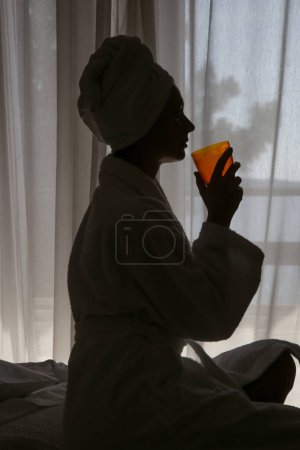 Foto de Joven hermosa mujer envuelta en toallas beber colágeno líquido o suplemento vitamínico al lado de la ventana, concepto de estilo de vida saludable por la mañana - Imagen libre de derechos