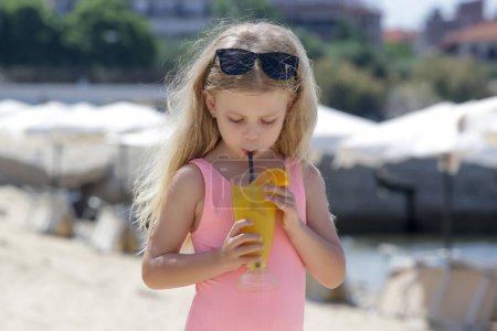Photo for Sdorable little girl having fresh squeezed orange juice in a beach bar, hydratation and healhy diet during hot summer days - Royalty Free Image