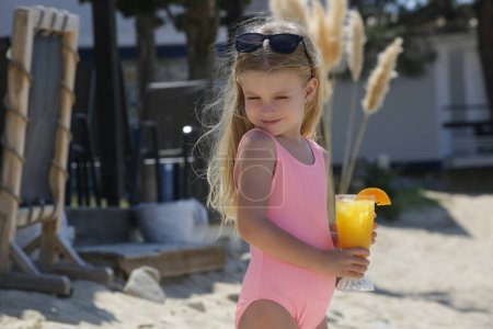 Photo for Adorable little girl having fresh squeezed orange juice in a beach bar, hydratation and healhy diet during hot summer days - Royalty Free Image
