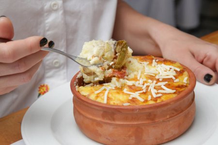 Woman eating traditional greek moussaka prepared in clay pot