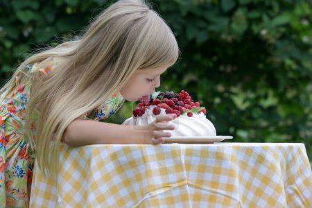 Téléchargez les photos : Adorable petite fille en robe d'été florale manger gâteau Pavlova - en image libre de droit
