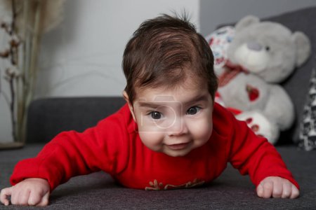 Téléchargez les photos : Portrait d'adorable nouveau-né en body rouge sur le canapé - en image libre de droit