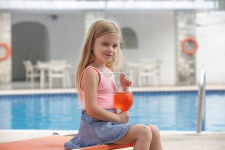 Photo for Adorable little girl having refreshment drinkby the poolside, hydratation and healhy diet during hot summer days - Royalty Free Image