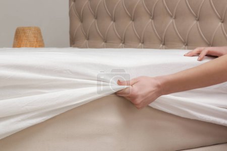 Foto de Cambiando sábanas. Mujer está poniendo en una sábana de algodón blanco ajustado en un colchón mientras hace la cama. - Imagen libre de derechos