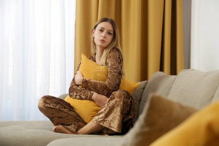 Photo for Young fashionable woman sitting on sofa and hugging a pillow, concept of autumn cozy lifesyle indoor, golden yellow colors, comfortable and stylish fall season plush outfit - Royalty Free Image