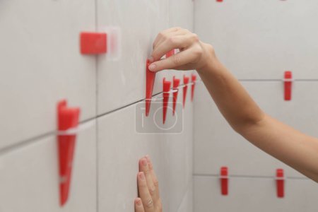 Photo for Woman tiling bathroom walls. Flat wall plastic tile leveling system. Process of installation of tiles in the bathroom. DIY home improvement. - Royalty Free Image