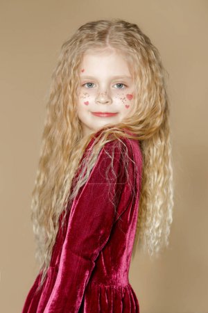 Photo for Portrait of cute little girl in red dress with long blonde hair and glitters and red hearts on the face - Royalty Free Image