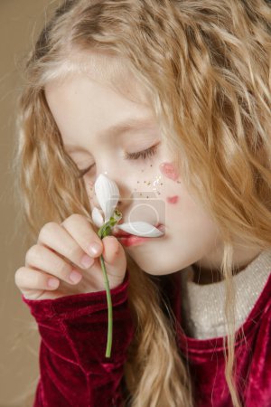 Photo for Portrait of cute little girl with glitters and red hearts on the face holding snowdrop flower - Royalty Free Image