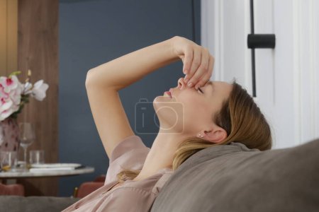Side view of woman with symptoms of frontal sinusitis, feeling of pressure between the eyes sitting on the sofa in the living room