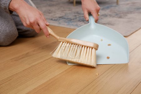Close up image of woman's hands cleaning apartment with small broom and dustpan