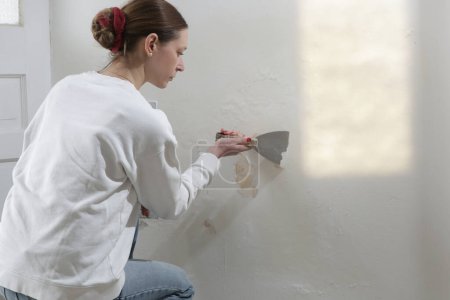 Téléchargez les photos : Salpêtre sur le problème du mur. Femme utilise un grattoir pour gratter et enlever toute la peinture en vrac et le plâtre qui est en mauvais état, jusqu'à ce qu'une surface ferme est atteinte. - en image libre de droit