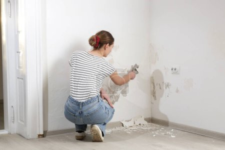 Salpêtre sur le problème du mur. Femme utilise un grattoir pour gratter et enlever toute la peinture en vrac et le plâtre qui est en mauvais état, jusqu'à ce qu'une surface ferme est atteinte.