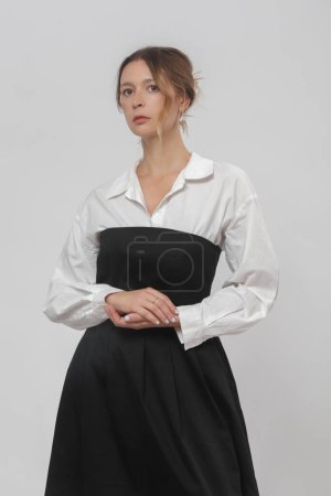 Serie of studio photos of female model wearing white button-down shirt under black tube top A line midi dress