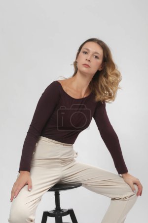Serie von Studiofotos des jungen weiblichen Modells in bequemem lässigem Basic-Outfit, weinrotem Viskose-Bootsausschnitt-Hemd und beiger Hose