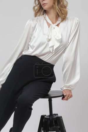 Fashion portrait of beautiful female model wearing elegant black trousers and white silk blouse on white background