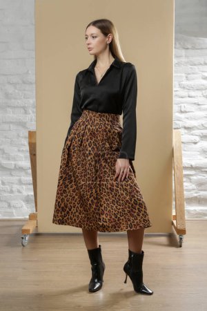 Serie de fotos de estudio de una joven modelo con blusa negra y falda midi con estampado animal. Moda cotidiana cómoda y elegante.