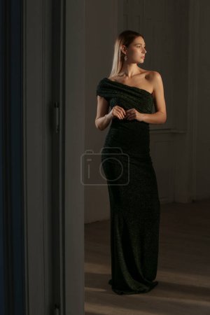 Indoor portrait of female model in elegant black sparkling one shoulder asymmetric dress