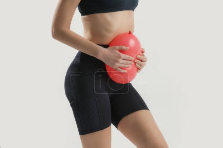 Junge Frau hält Luftballon als Zeichen einer Magenaufblähung, Blähungen und Menstruationskrämpfe 