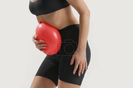 Young woman holding balloon as a sign of an stomach inflation, bloating and menstrual cramps concept 