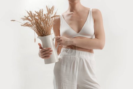 Téléchargez les photos : Jeune femme tenant pichet en céramique avec bouquet de pointes de blé, la maladie coeliaque et l'intolérance au gluten - en image libre de droit