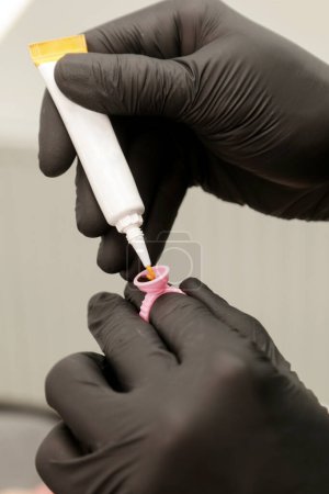 Artista de Microblading en guantes negros mezclando pigmento en taza de anillo de tinta. Primer plano del envase del anillo del pigmento y de la tinta para el tatuaje de la ceja. Preparación del procedimiento de belleza.