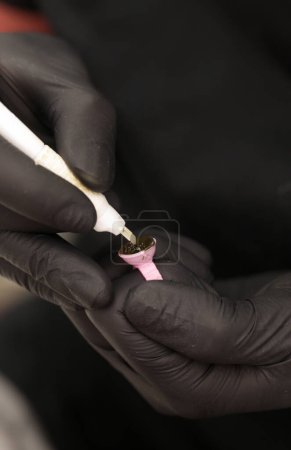 Artista de Microblading en guantes negros mezclando pigmento en taza de anillo de tinta. Primer plano del envase del anillo del pigmento y de la tinta para el tatuaje de la ceja. Preparación del procedimiento de belleza.