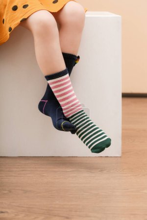 Kid wears different pair of socks. Child foots in mismatched socks, studio photography. Down syndrome awareness concept, odd socks day, anti-bullying week.