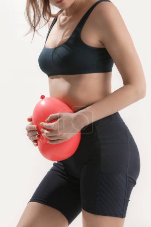 Young woman holding balloon as a sign of an stomach inflation, bloating and menstrual cramps concept