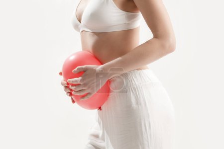 Junge Frau hält Luftballon als Zeichen einer Magenaufblähung, Blähungen und Menstruationskrämpfe