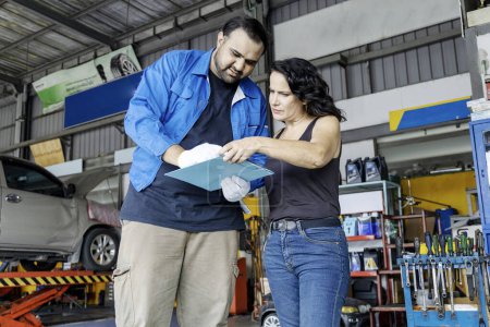 Photo for Mechanic holding a clipboard and showing the car checking list and repaired item to woman customer in the garage, Auto car repair service center, Professional service, Selective Focus - Royalty Free Image