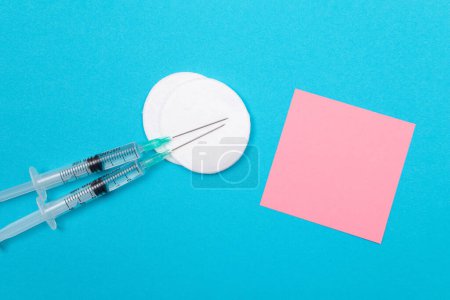 Photo for Vaccination, Immunology or Revaccination Concept - Two Medical Disposable Syringe Lying on Blue Table in Doctors Office in a Hospital or Clinic. Blank Pink Sticky Note - Mock Up with Copy Space - Royalty Free Image