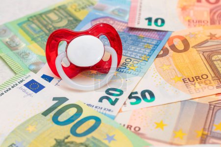 Foto de Childfree, Anticoncepción and Birth Control Concept: Baby Pacifier on the Euro Banknotes (en inglés). Tener hijos es caro y poco rentable - Imagen libre de derechos