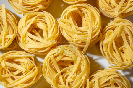Ungekochte Fettuccine Pasta auf Eierbasis: Eine kulinarische Leinwand aus bandförmigen Makkaroni, die einen lebendigen und strukturierten Hintergrund für die Gourmetküche schafft. Trockene Pasta. Rohe Makkaroni - Ansicht von oben, flach gelegt