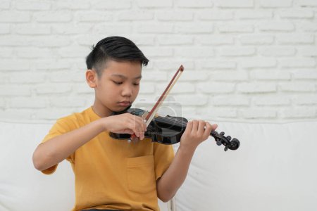 Téléchargez les photos : A Little Asian kid playing and practice violin music string instrument against in home, Concept d'éducation musicale, Inspiration, Étudiante en école d'art. - en image libre de droit