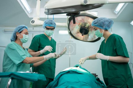 Téléchargez les photos : Équipe de chirurgiens professionnels asiatiques effectuant une chirurgie dans la salle d'opération, chirurgien, assistants et infirmières effectuant une chirurgie sur un patient, concept de traitement du cancer et de la maladie des soins de santé - en image libre de droit