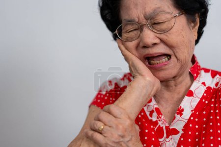 Asia old senior woman suffering from severe toothache, holding her cheek and suffering strong dental pain on white background, tooth decay, tooth sensitivity, oral health care concept.