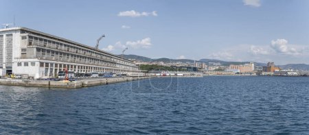 Téléchargez les photos : TRIESTE, ITALIE - 29 mai 2023 : Paysage urbain avec des bâtiments portuaires et une myriade de truques et d'autocars bordés sur le quai, tourné de la mer sous une lumière vive le 29 mai 2023 à Trieste, Frioul, Italie - en image libre de droit