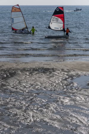 Photo for CASTIGLIONE DELLA PESCAIA, 2023 oct 01: glittering sand and participants landing boats in shallow water at the end of Open Skiff National regatta at sea village, shot in bright  early fall light on oct 01, 2023 at Castiglione della Pescaia, Italy, - Royalty Free Image