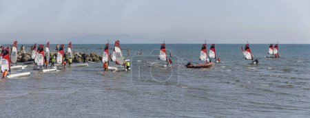 Photo for CASTIGLIONE DELLA PESCAIA, 2023 oct 01: participants collecting boats amid glittering sand and water at the end of Open Skiff National regatta at sea village, shot in bright  early fall light on oct 01, 2023 at Castiglione della Pescaia,  Italy - Royalty Free Image