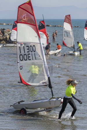 Photo for CASTIGLIONE DELLA PESCAIA, 2023 oct 01: female contestant pulling her boat out of shallow water at the end of Open Skiff National regatta at sea village, shot in bright  early fall light on oct 01, 2023 at Castiglione della Pescaia, Tuscany, Italy - Royalty Free Image