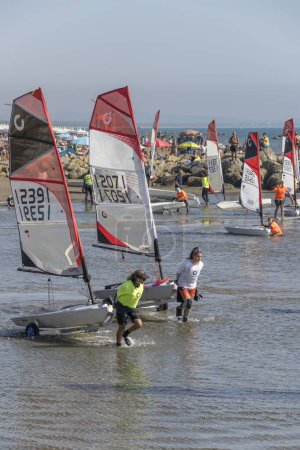 Photo for CASTIGLIONE DELLA PESCAIA, 2023 oct 01: participants collecting boats amid glittering sand and water at the end of Open Skiff National regatta at sea village, shot in bright  early fall light on oct 01, 2023 at Castiglione della Pescaia,  Italy - Royalty Free Image