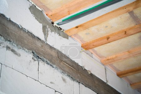 Photo for Poorly poured concrete armored belt in an aerated concrete wall. The bare walls of an unfinished house made of aerated concrete bricks and a glass wool insulated ceiling lined with a vapor barrier. - Royalty Free Image