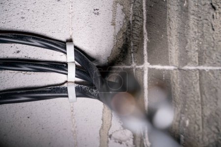 Photo for Three black power wires are attached in parallel to an aerated concrete brick. Electrical wiring in the wall of the gas block close-up - Royalty Free Image