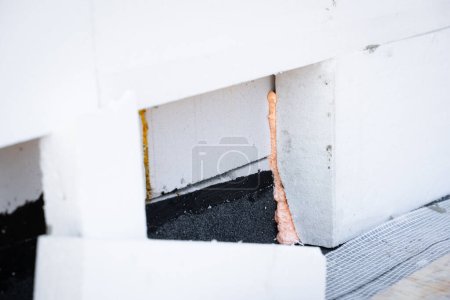 The process of insulating a house with polystyrene foam insulation. A thick sheet of white foam is glued to the wall with construction spray foam
