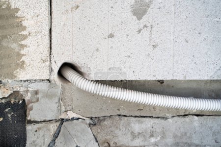 Foto de El alambre en un tubo corrugado plástico protector se coloca a través de la pared a través de un agujero en el ladrillo de hormigón aireado. Conducción de electricidad a la casa. Agujero perforado en bloque de gas - Imagen libre de derechos