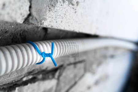 Foto de Fastening wiring in a corrugated pipe to the wall with a blue clamp close-up. Outdoor street electrical wiring on a blurred background - Imagen libre de derechos