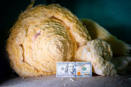 Photo for One hundred dollars lie near a roll of glass wool close-up. Cash on the phonet of building materials for insulation and soundproofing. Rising prices for building materials. Purchase of mineral glass wool - Royalty Free Image
