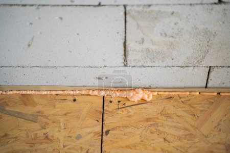 Téléchargez les photos : L'espace entre le plancher de la dalle OSB et le mur en béton aéré est rempli de mousse de construction. Hydrobarrière sous un plancher de bois rugueux - en image libre de droit