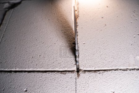 Téléchargez les photos : Le processus de coupe à travers un mur à partir d'un bloc de béton aéré avec une scie à main pour le béton aéré gros plan sur un fond flou. Réaménagement de la maison et la coupe d'une porte dans le mur - en image libre de droit