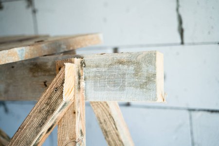 Téléchargez les photos : Wooden homemade scaffolding close-up against the background of a bare aerated concrete wall - en image libre de droit